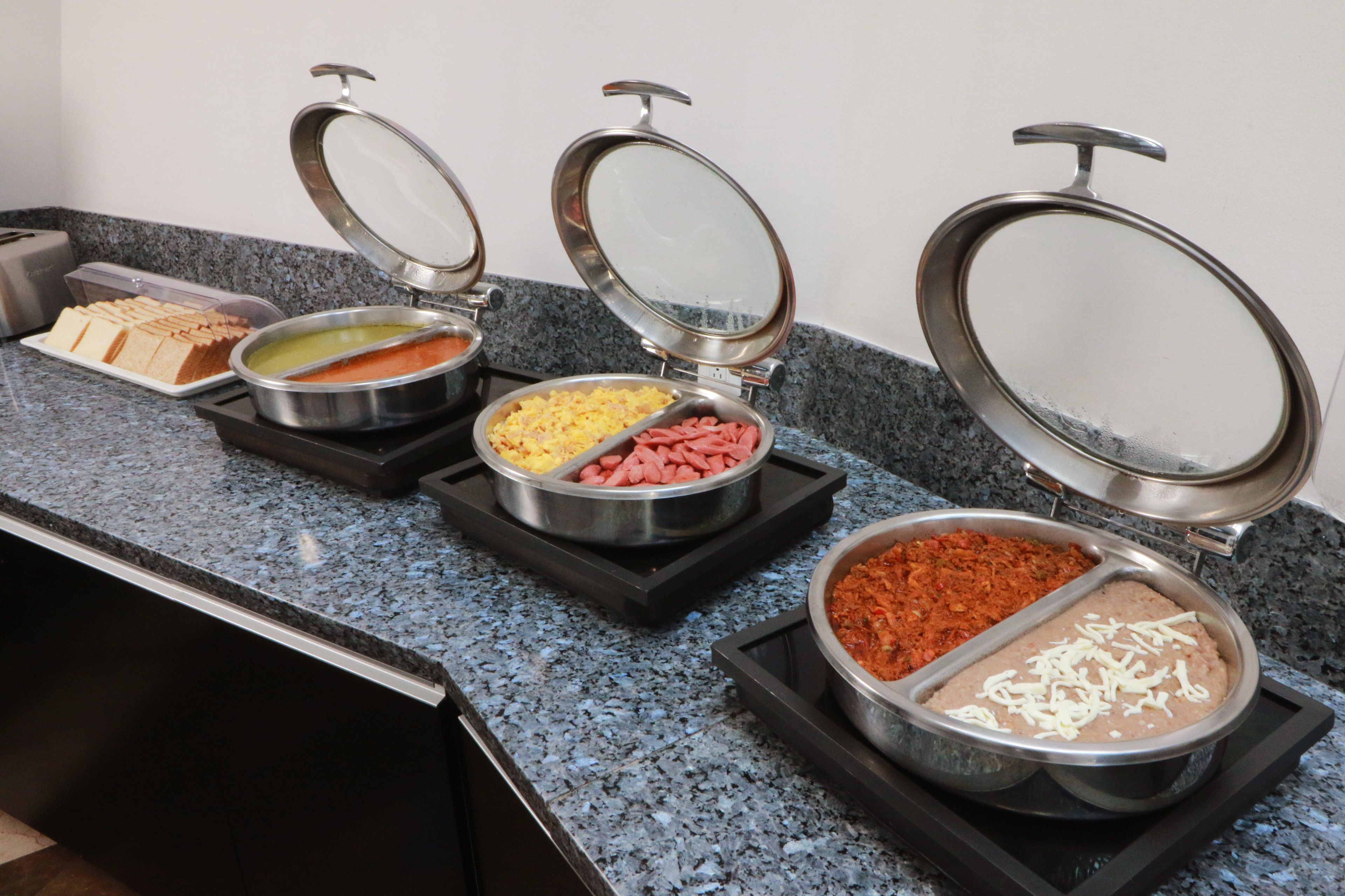 Un bufé con diferentes alimentos en recipientes metálicos sobre una encimera de granito.