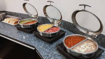 Un bufé con diferentes alimentos en recipientes metálicos sobre una encimera de granito.