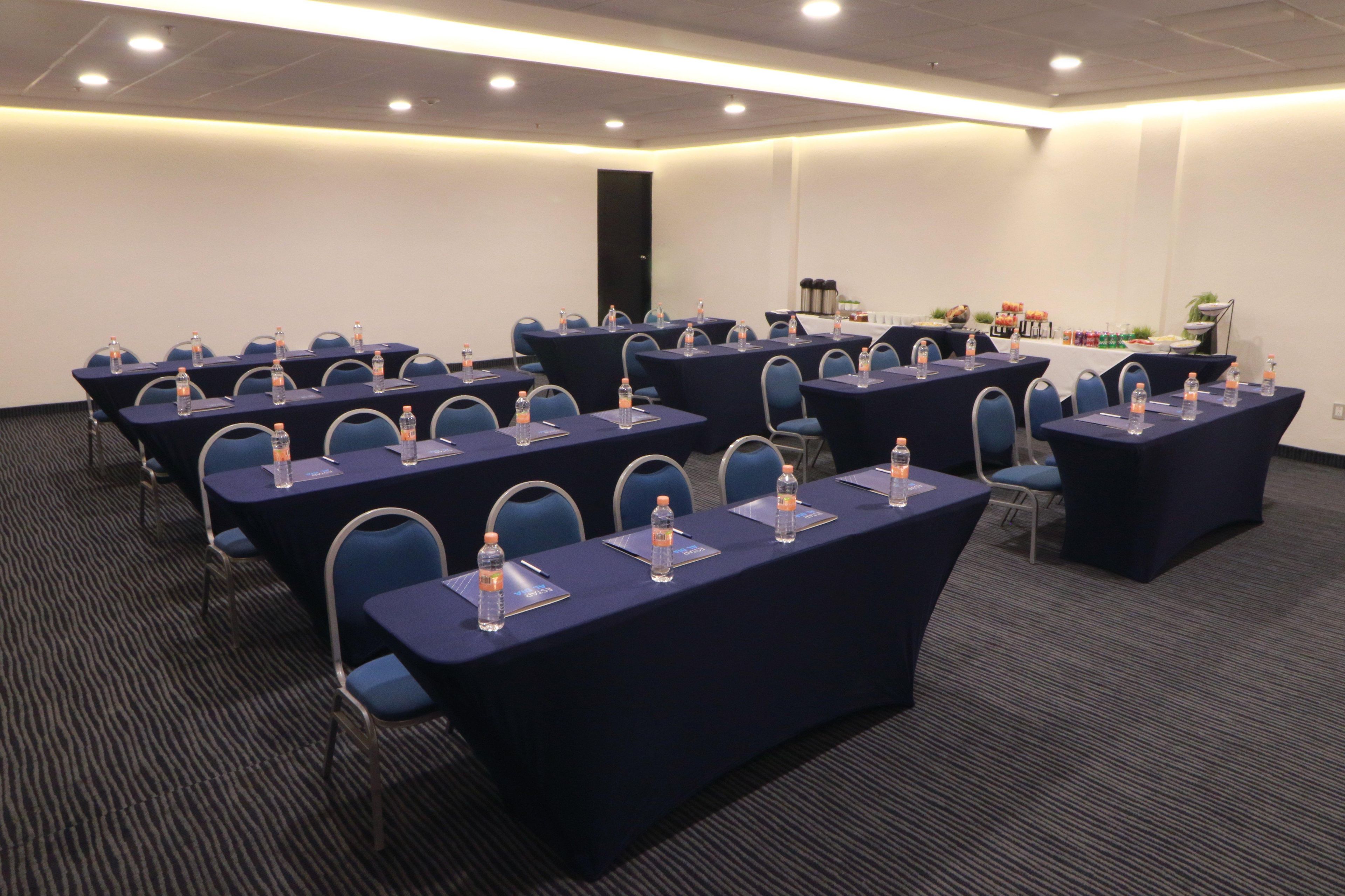 A conference room with multiple tables, chairs, and water bottles.