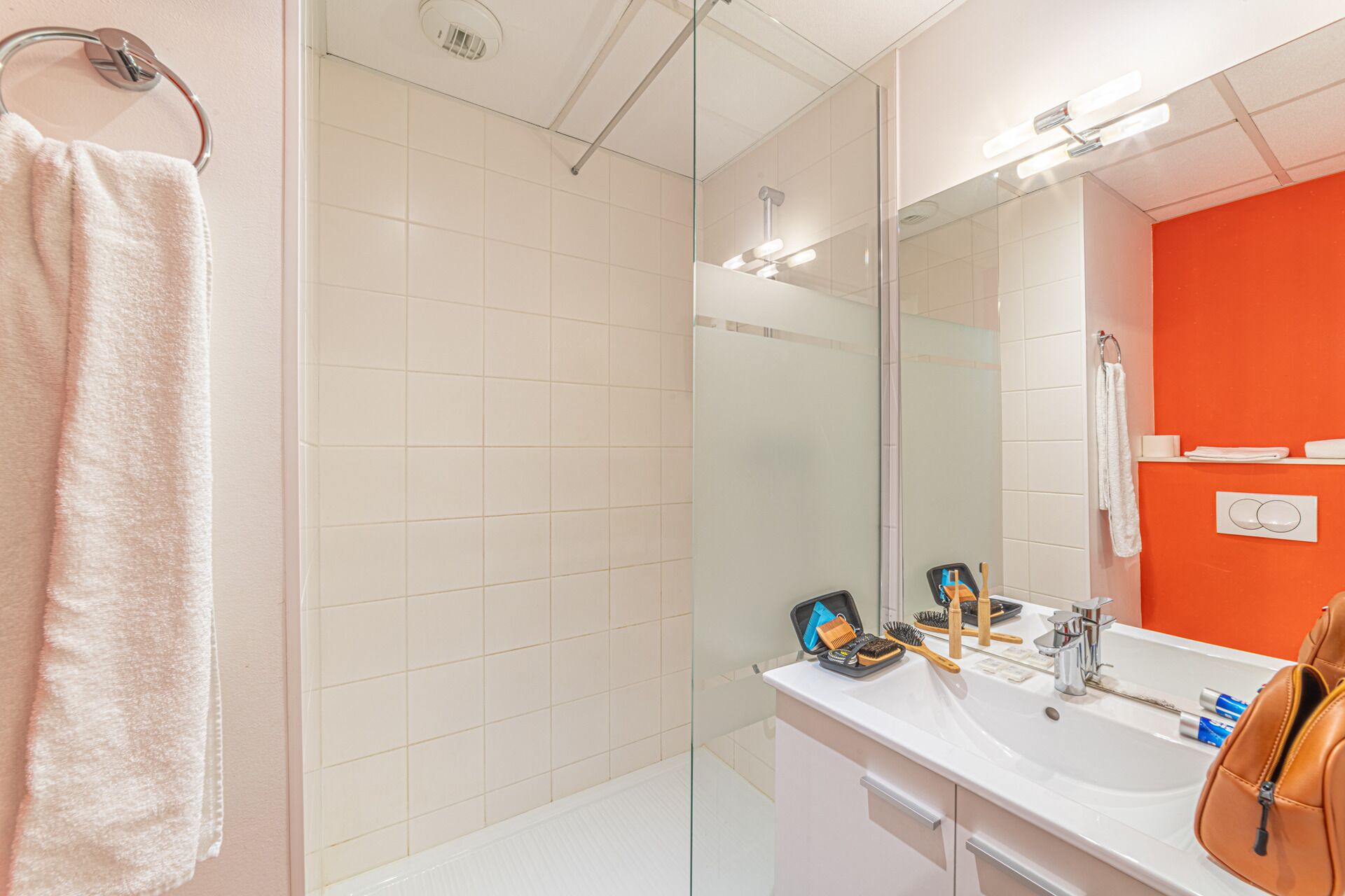 Un baño moderno con cabina de ducha de vidrio, un lavabo blanco con artículos de aseo y un espejo grande.