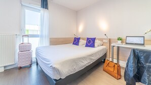 Ein Hotelzimmer mit einem Bett, einem Schreibtisch mit Laptop, einem Koffer und einer Jacke.