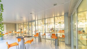 Ein moderner Innenraum mit Glaswänden, orangefarbenen Stühlen und Tischen.