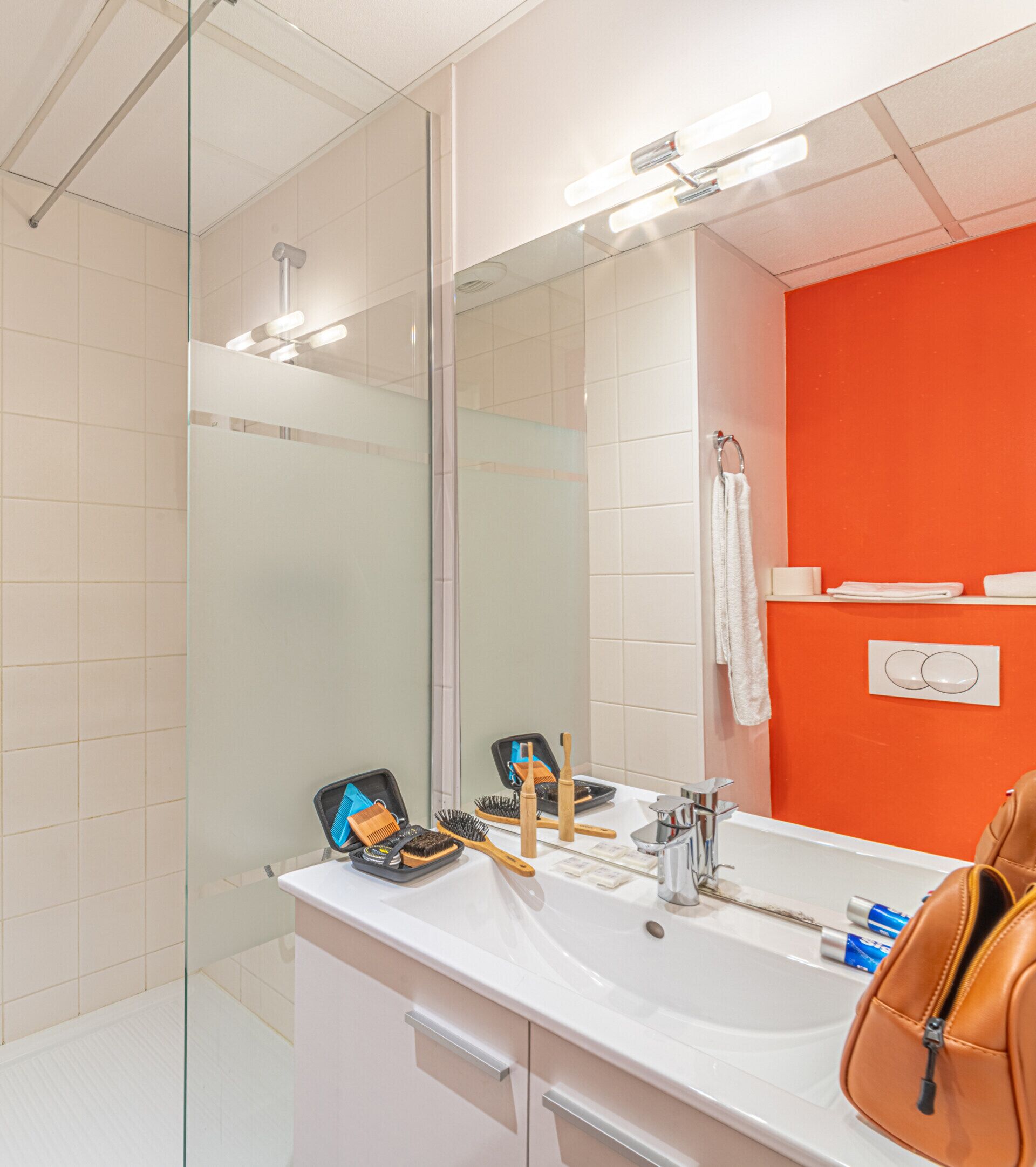 A modern bathroom with a large mirror, a white sink, and a glass shower enclosure.
