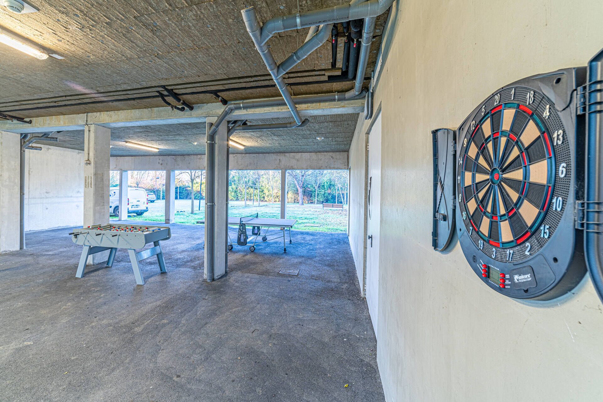 A covered indoor area with a dartboard, a foosball table, and a ping pong table.