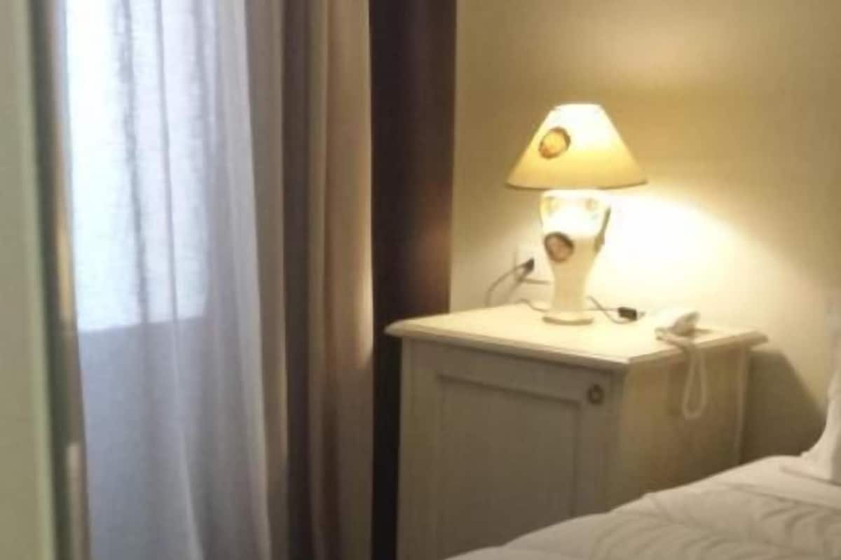 Een hotelkamer met een bed, een nachtkastje met een lamp en een raam met gordijnen.