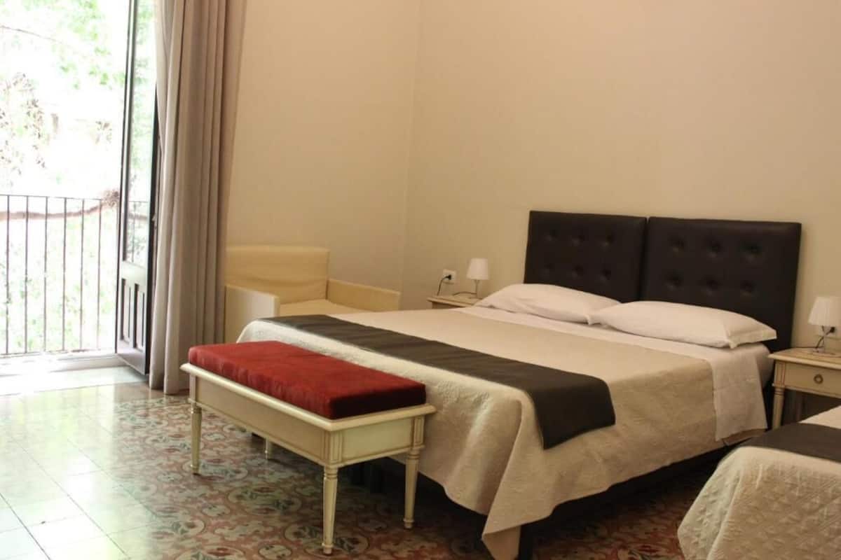 Een hotelkamer met een bed, nachtkastje, bankje en uitzicht op het groen.