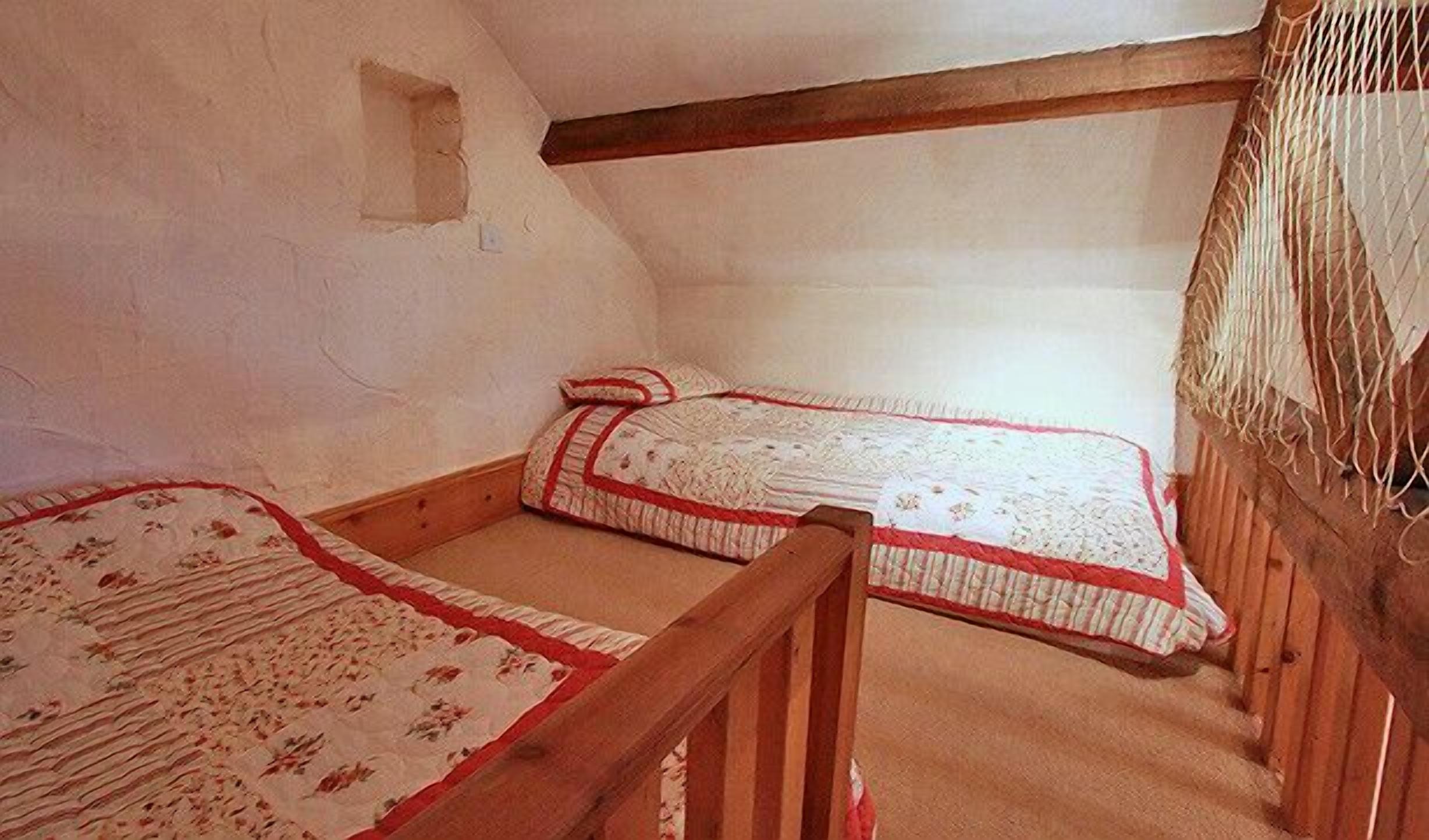 A small, rustic room with two wooden bunk beds, a sloped ceiling, and a small window.