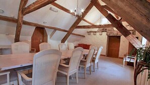 A dining area with a high ceiling and exposed wooden beams, featuring a long table and white wicker chairs. - Centre of Britain Hotel & Restaurant (Haltwhistle)