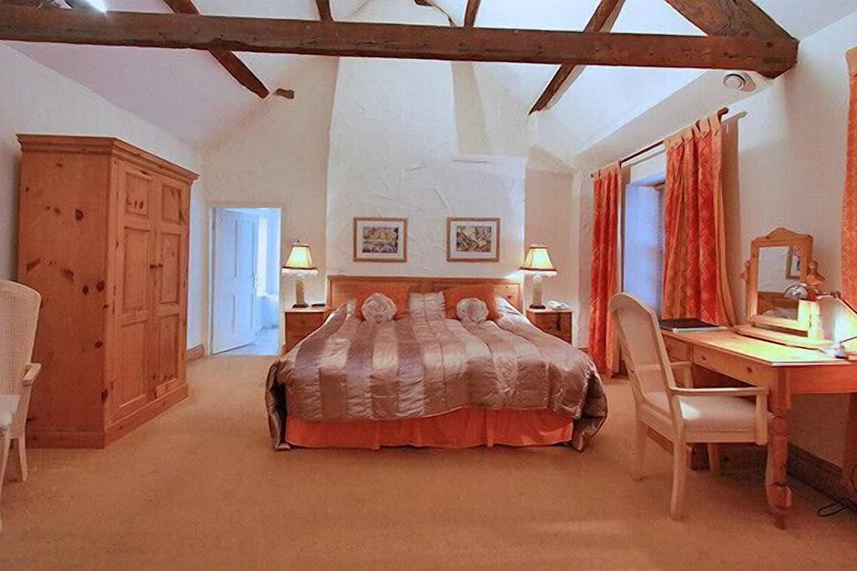 A bedroom with a large bed, a desk with a chair, a wardrobe, and a mirror.