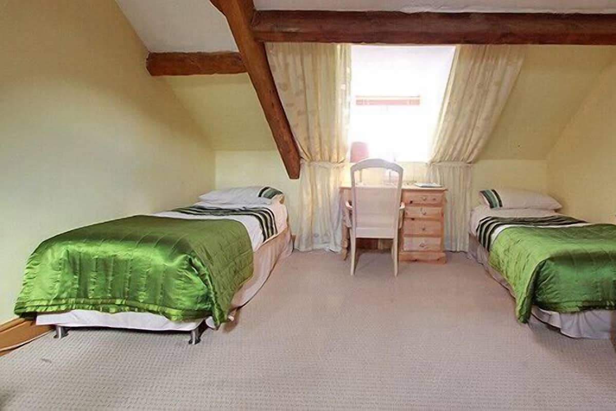 A small, cozy room with two single beds, a desk, and a chair.
