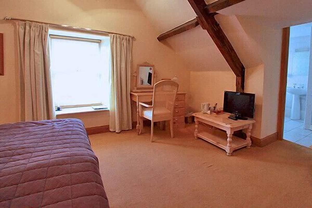 A bedroom with a bed, a desk, a chair, a television, and a window with curtains.