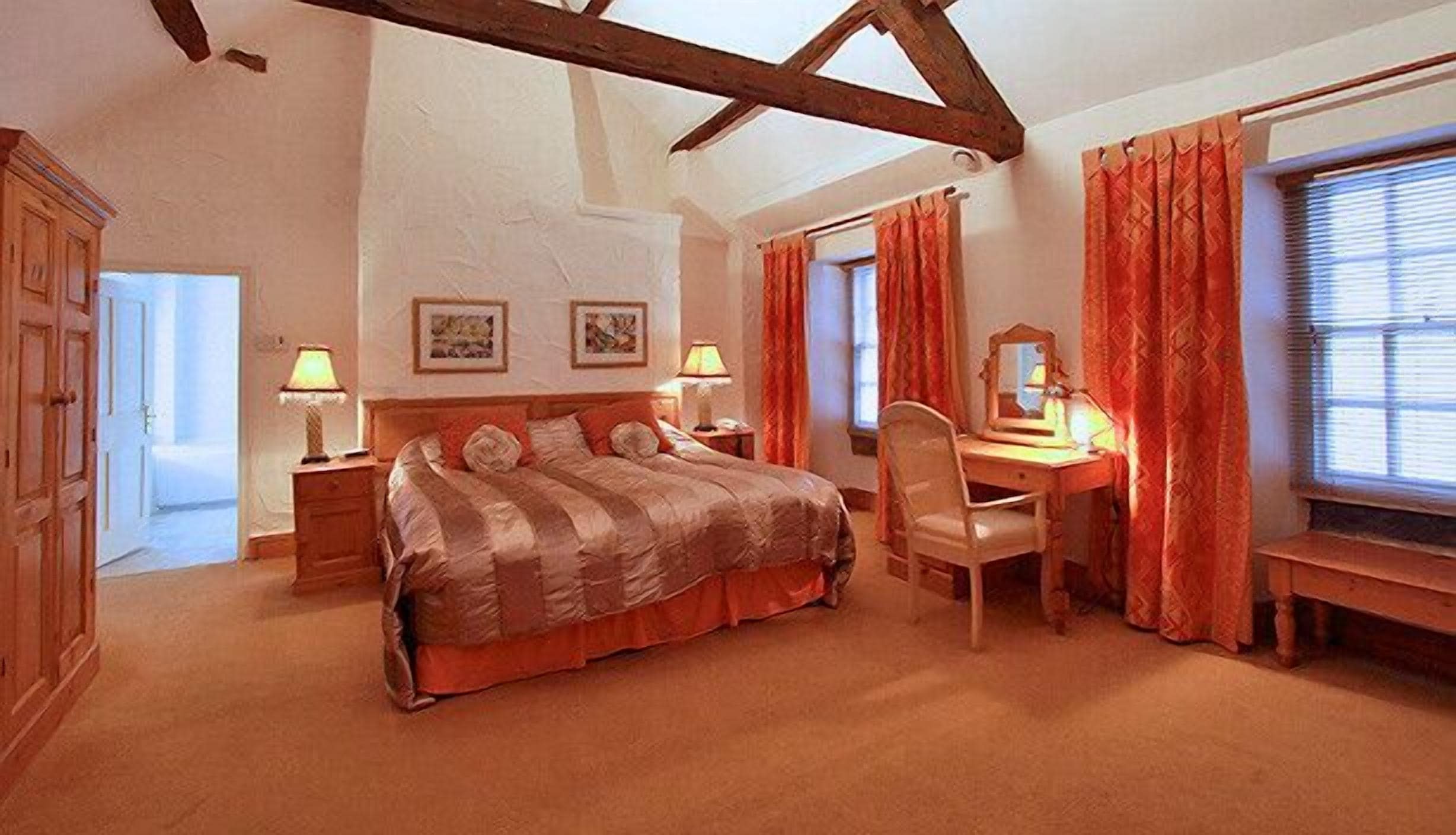A bedroom with a large bed, a desk with a chair, and a window with curtains.