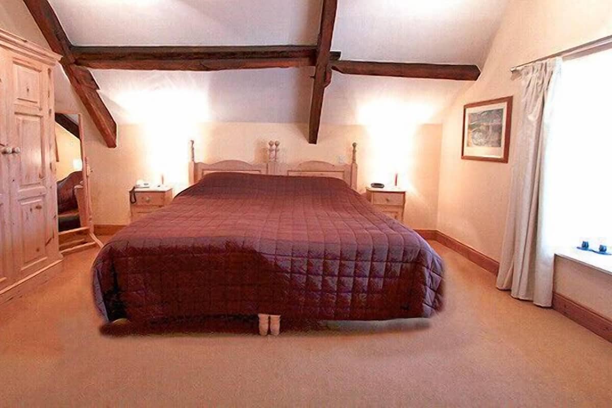 A bedroom with a large bed, wooden wardrobe, and a nightstand.