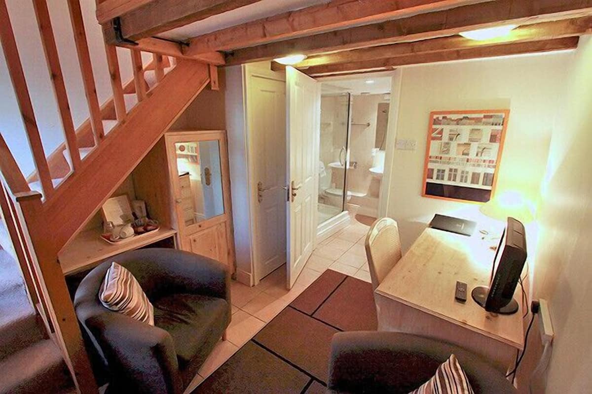 A cozy room with a wooden staircase, a small seating area with a table and chairs, and a shower area visible through an open door.