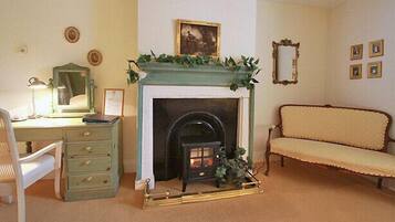 A room with a fireplace, a desk with a lamp, a chair, and a sofa.