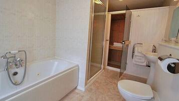 Un baño con bañera, inodoro y zona de ducha con mampara de vidrio.