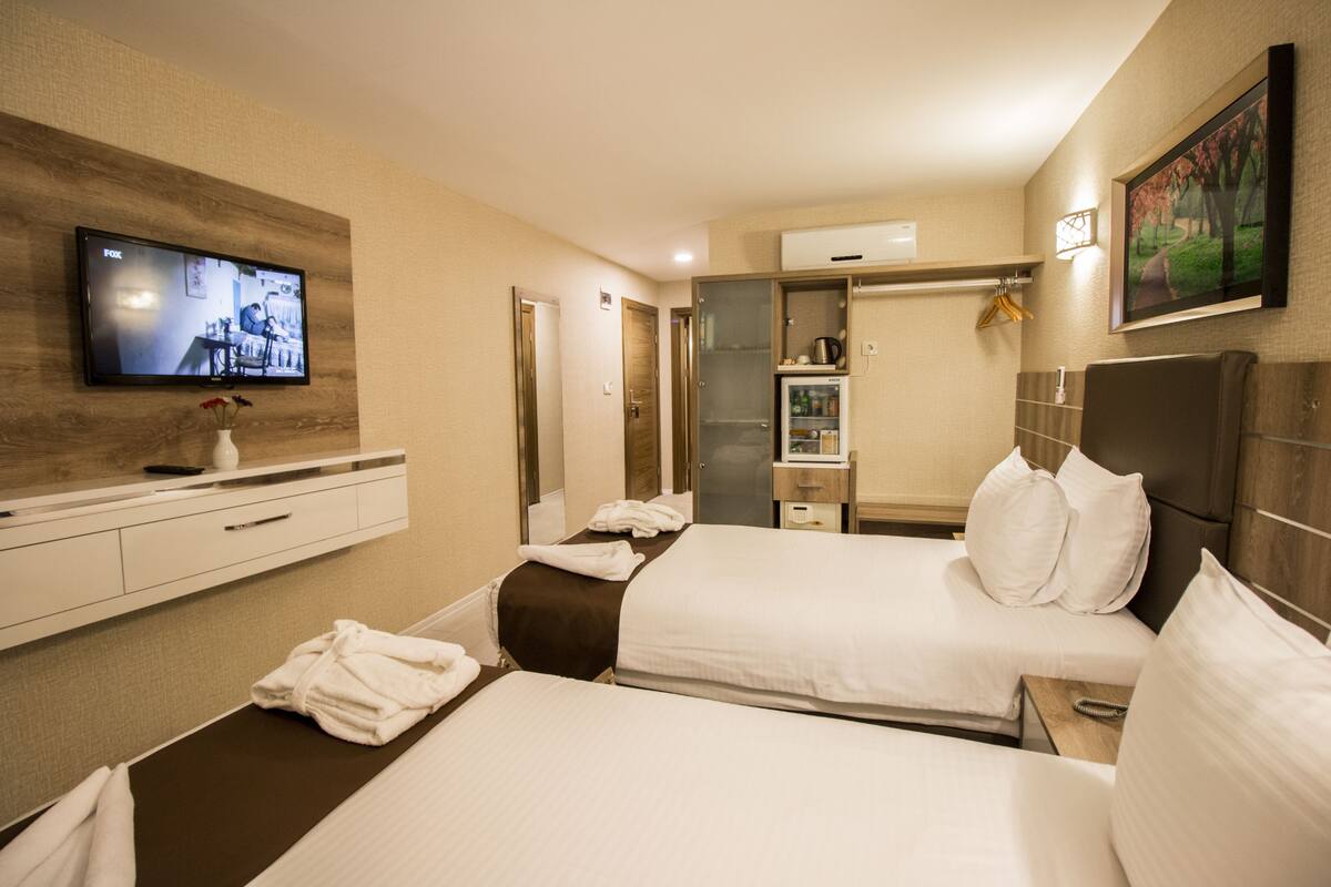 Habitación de hotel con dos camas, televisión montada en la pared, minibar y un cuadro decorativo.