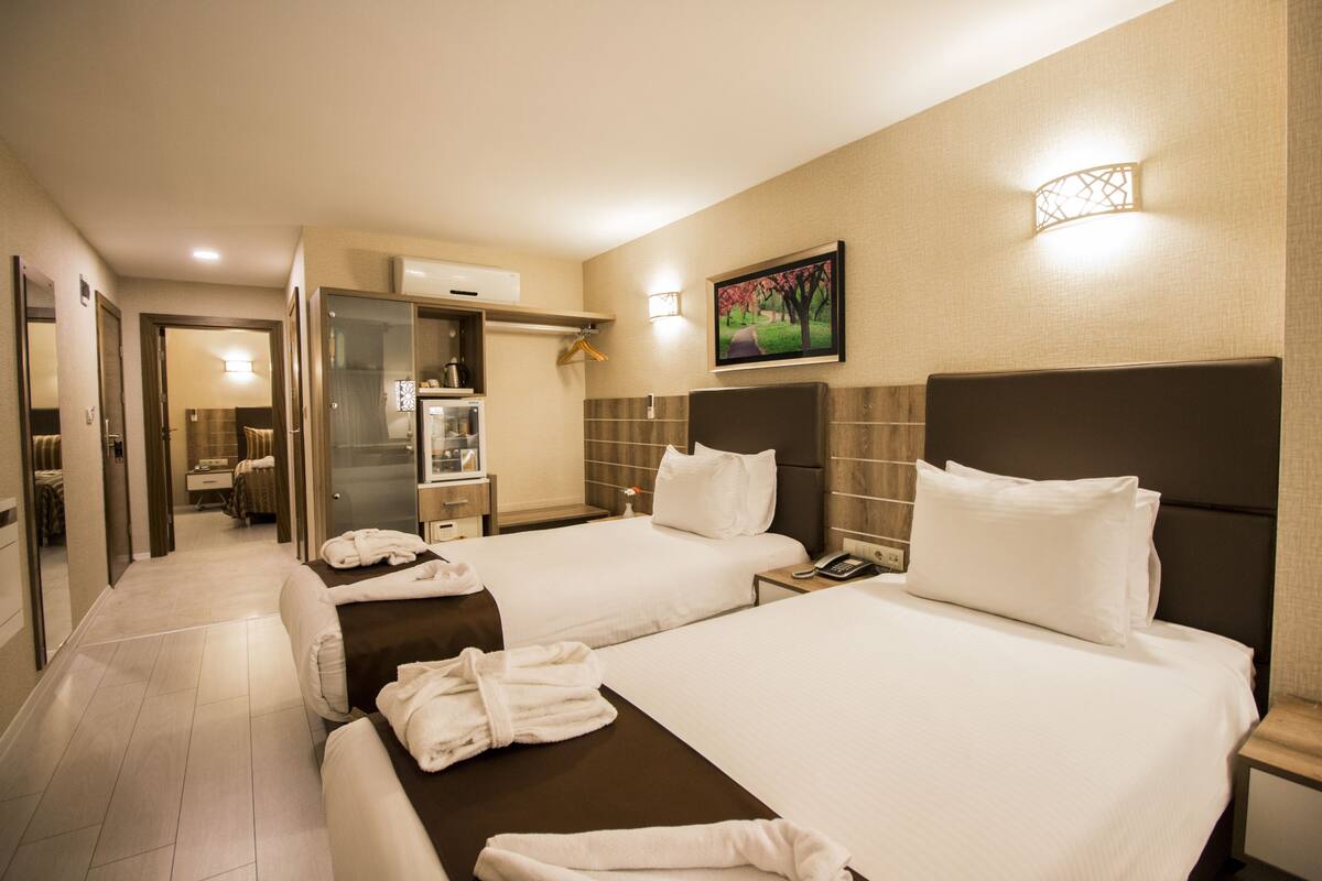 Habitación de hotel con dos camas, un baño y un pasillo que conduce a otra habitación.