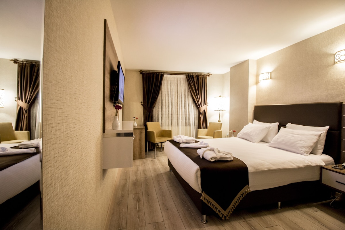 A hotel room with a large bed, bedside tables, a desk, a chair, and a television.