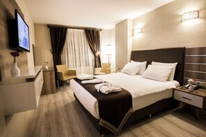 Una habitación de hotel moderna con una cama grande, mesitas de noche, un televisor y una zona de estar con una silla y una pequeña mesa.