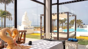 Habitación con vista a Playa Budha, una estatua de Buda, una mesa de masajes y una pequeña mesa blanca con un cojín azul.