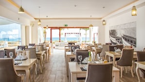 Un restaurante con mesas y sillas dispuestas para comer, vista al océano y un cuadro en la pared.