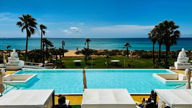 Un área de piscina con sillones de descanso y sombrillas, con vista despejada a la playa y al océano.