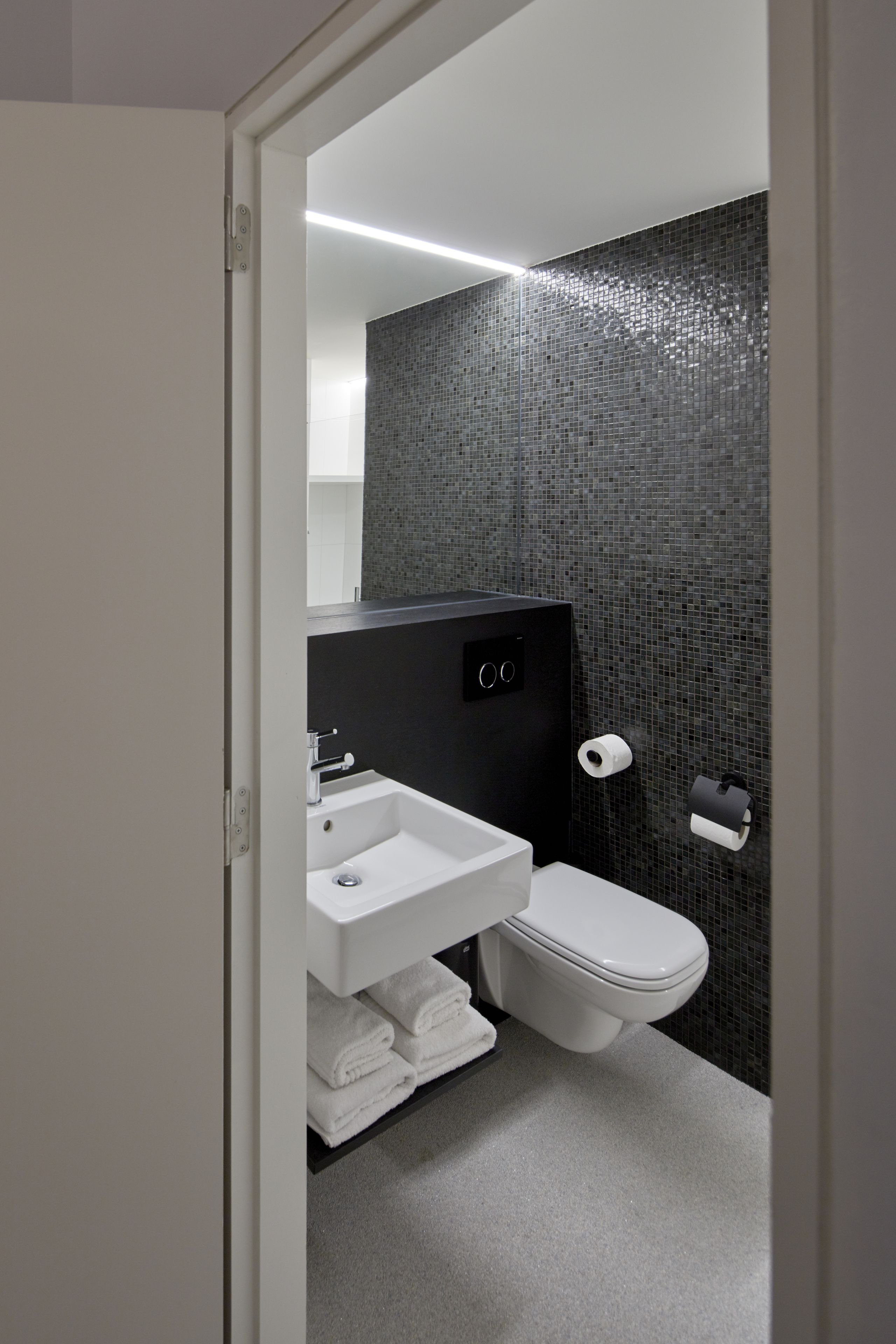 A modern bathroom with a white sink, toilet, and dark tiled walls.