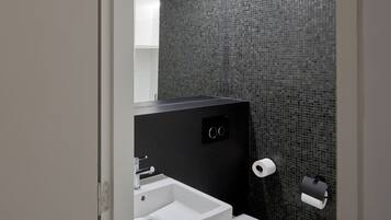 A modern bathroom with a white sink, toilet, and dark tiled walls.