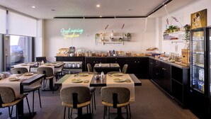 Un espace repas moderne avec des tables disposées pour accueillir quatre personnes, un néon et un réfrigérateur rempli de boissons.