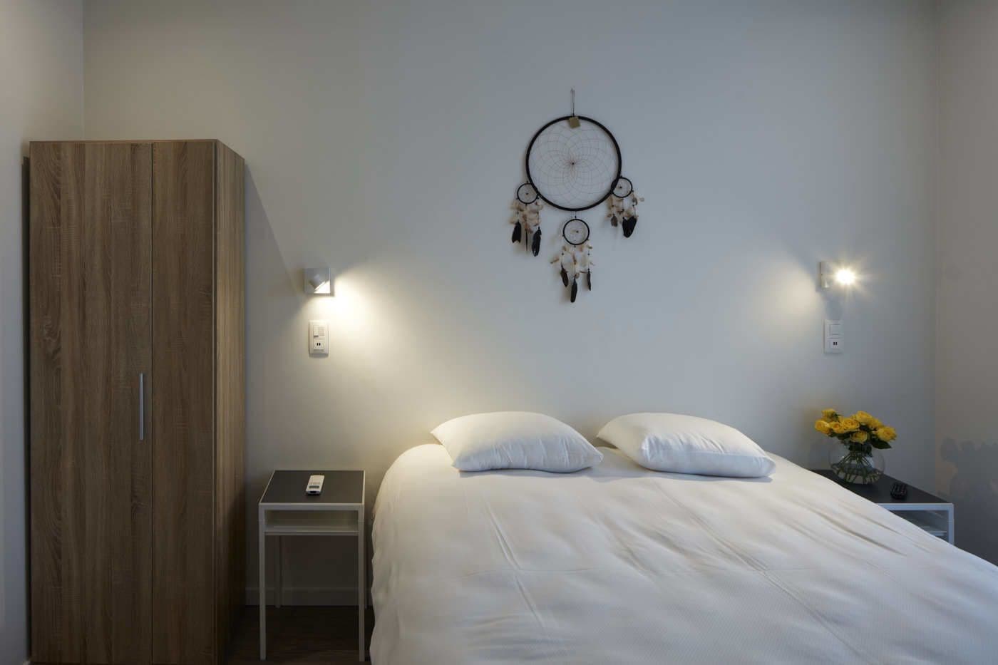 Une chambre à coucher comprenant un lit, des tables de chevet, une armoire, un attrape-rêves, des appliques murales et un vase avec des fleurs.