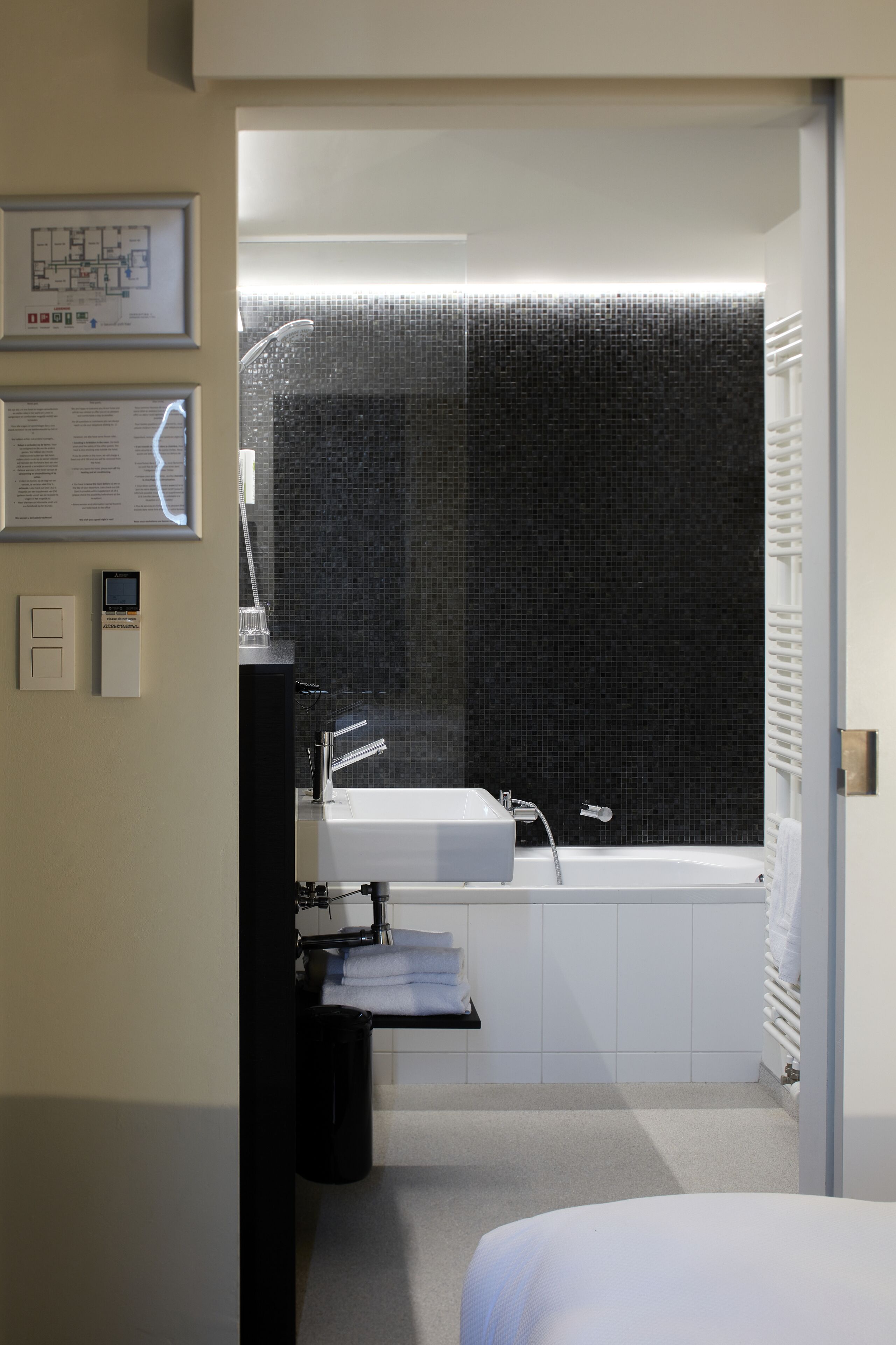 Ein modernes Badezimmer mit einem weißen Waschbecken, einer Badewanne und einem Duschbereich. An der Wand hängt eine gerahmte Karte und ein kleiner Mülleimer steht bereit.