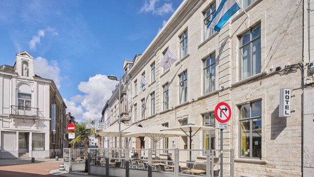 Un hôtel doté d’une façade traditionnelle en pierre, d’un espace extérieur aménagé avec des parasols et d’un panneau indiquant qu’il est interdit de se garer.