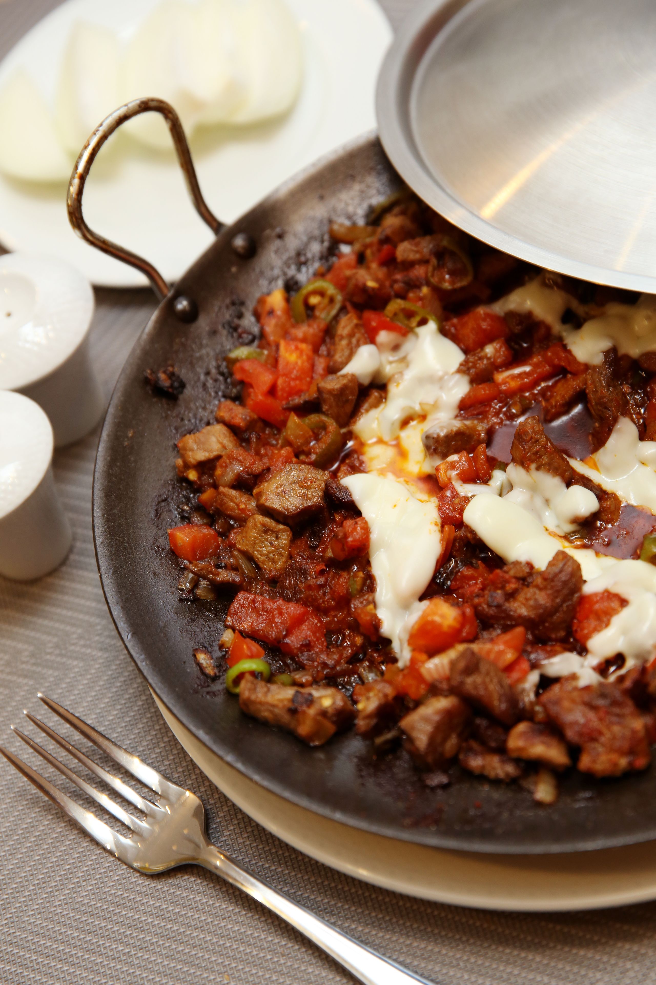 A pan with a dish containing meat and vegetables, a fork, and a plate with a lid.