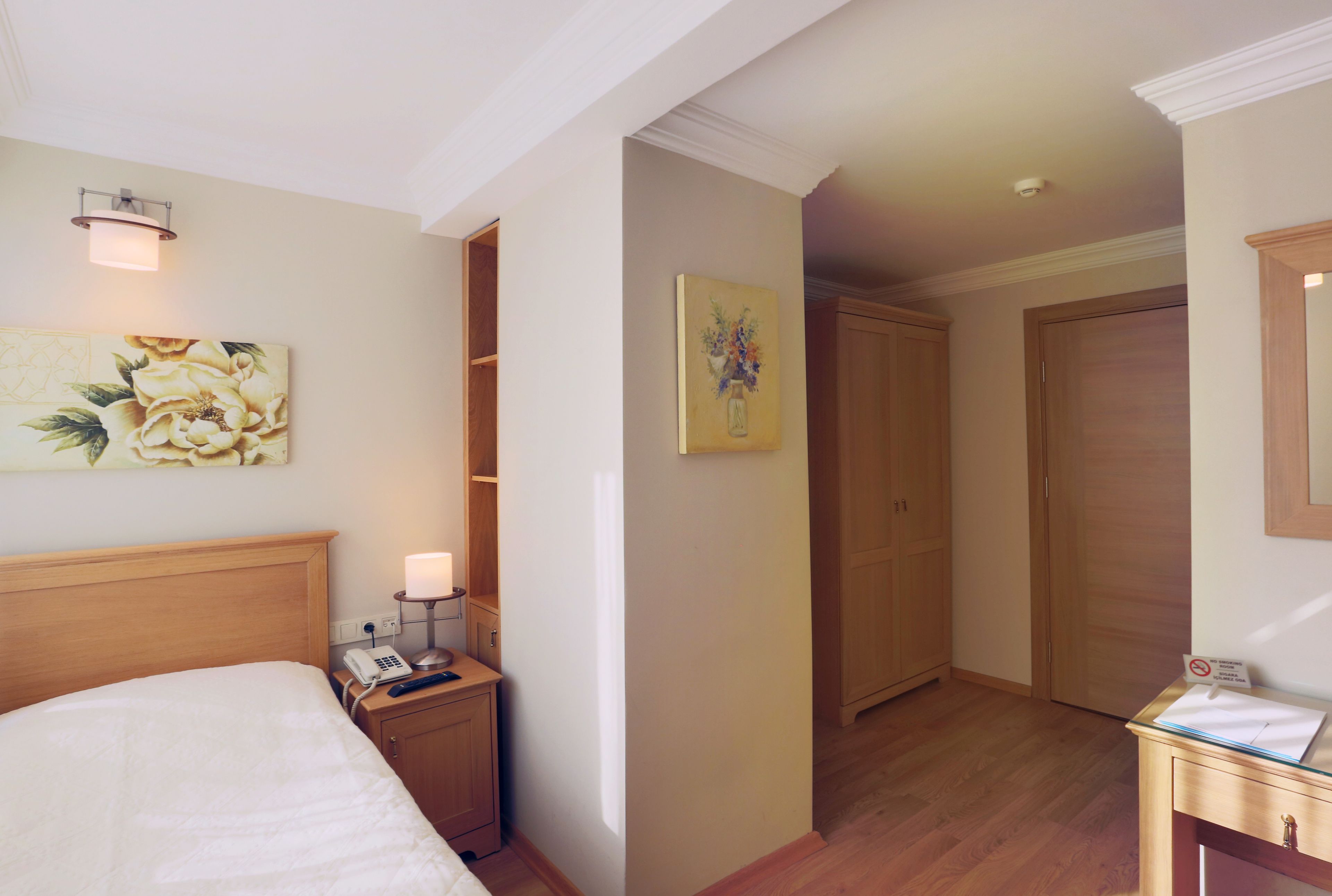 Ein Hotelzimmer mit einem Bett, einem Nachttisch mit Lampe, einem Telefon, einem Bild an der Wand und einem Holzschrank.