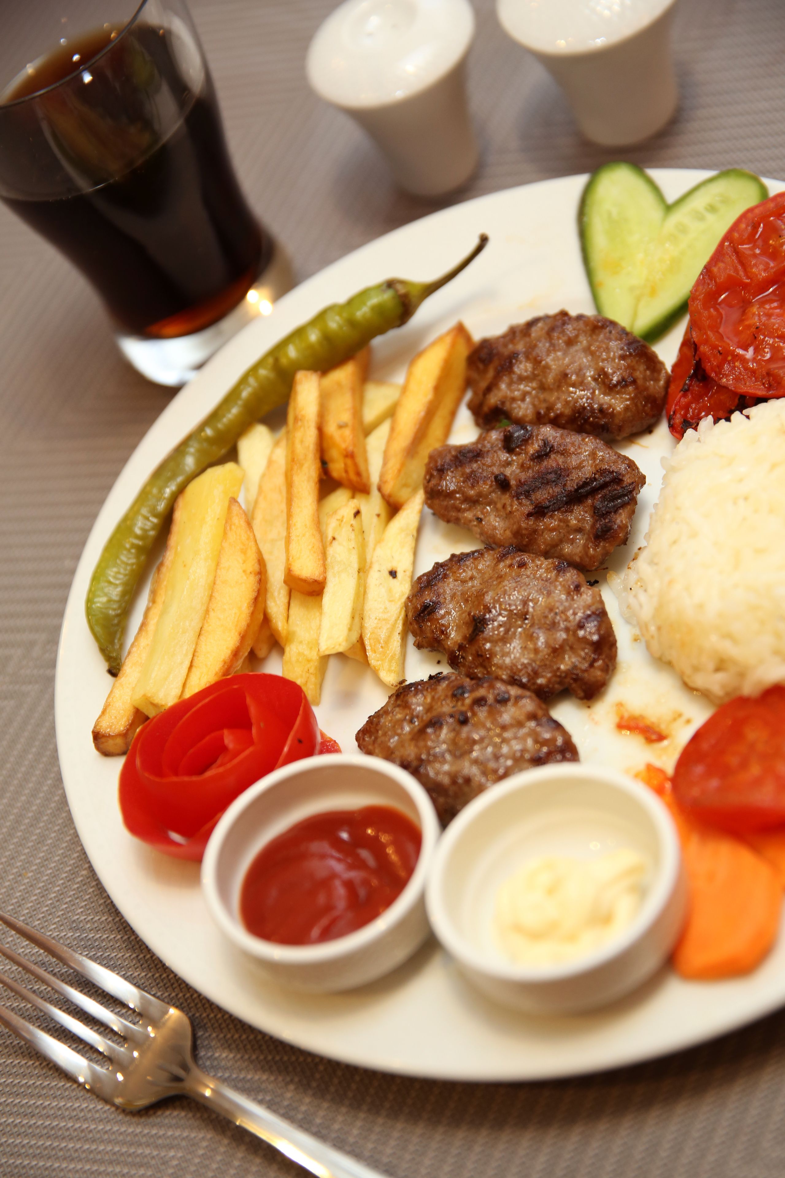 A plate of food with fries, meat, rice, and vegetables.