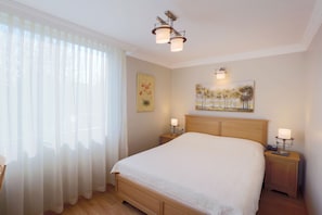 Camera da letto con un letto grande, due comodini, una lampada a sospensione e una finestra con tende leggere.