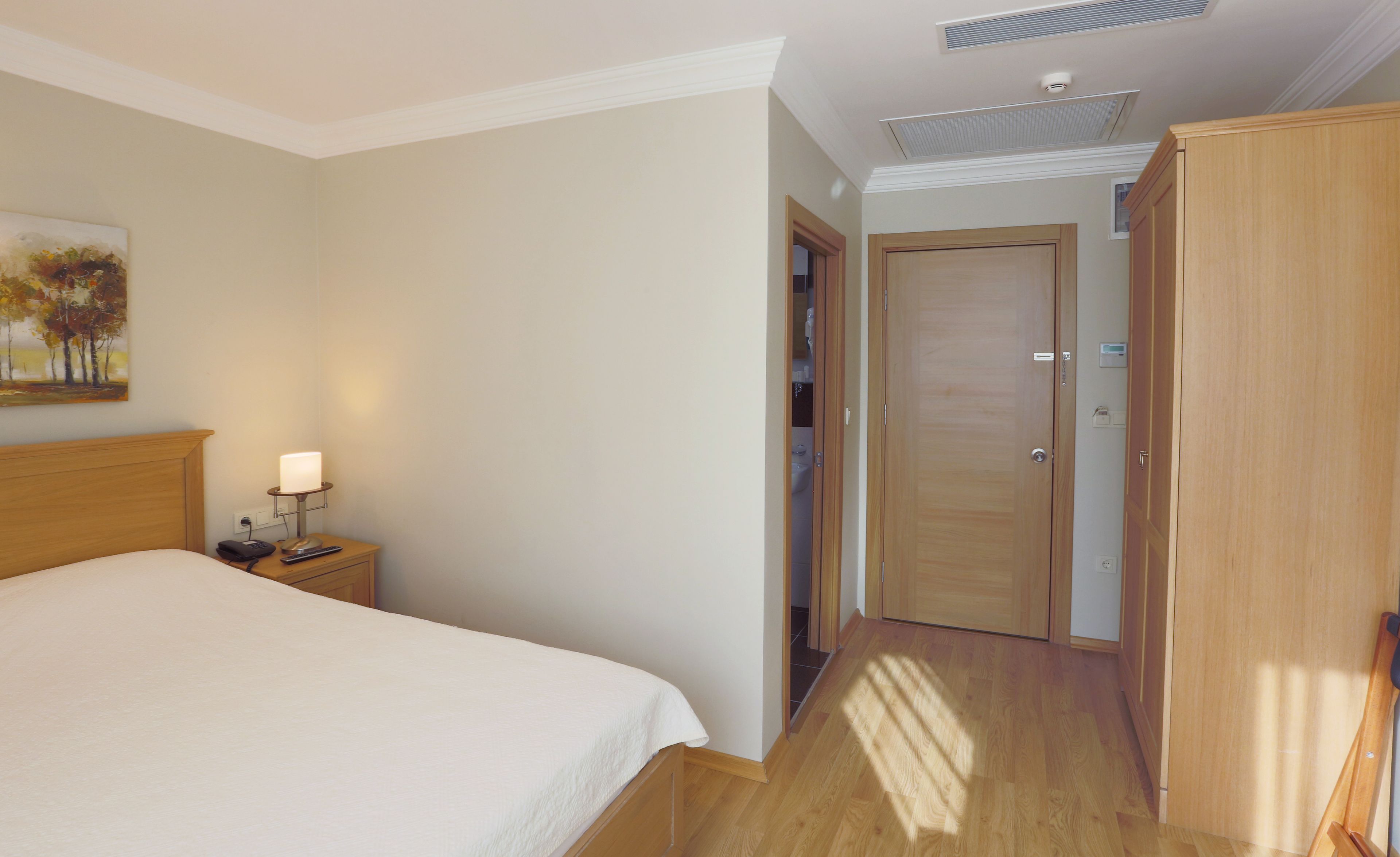 A hotel room with a bed, bedside table, lamp, and a painting on the wall.