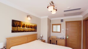 Une chambre d’hôtel avec un grand lit, un bureau, une chaise, un tableau et une porte.