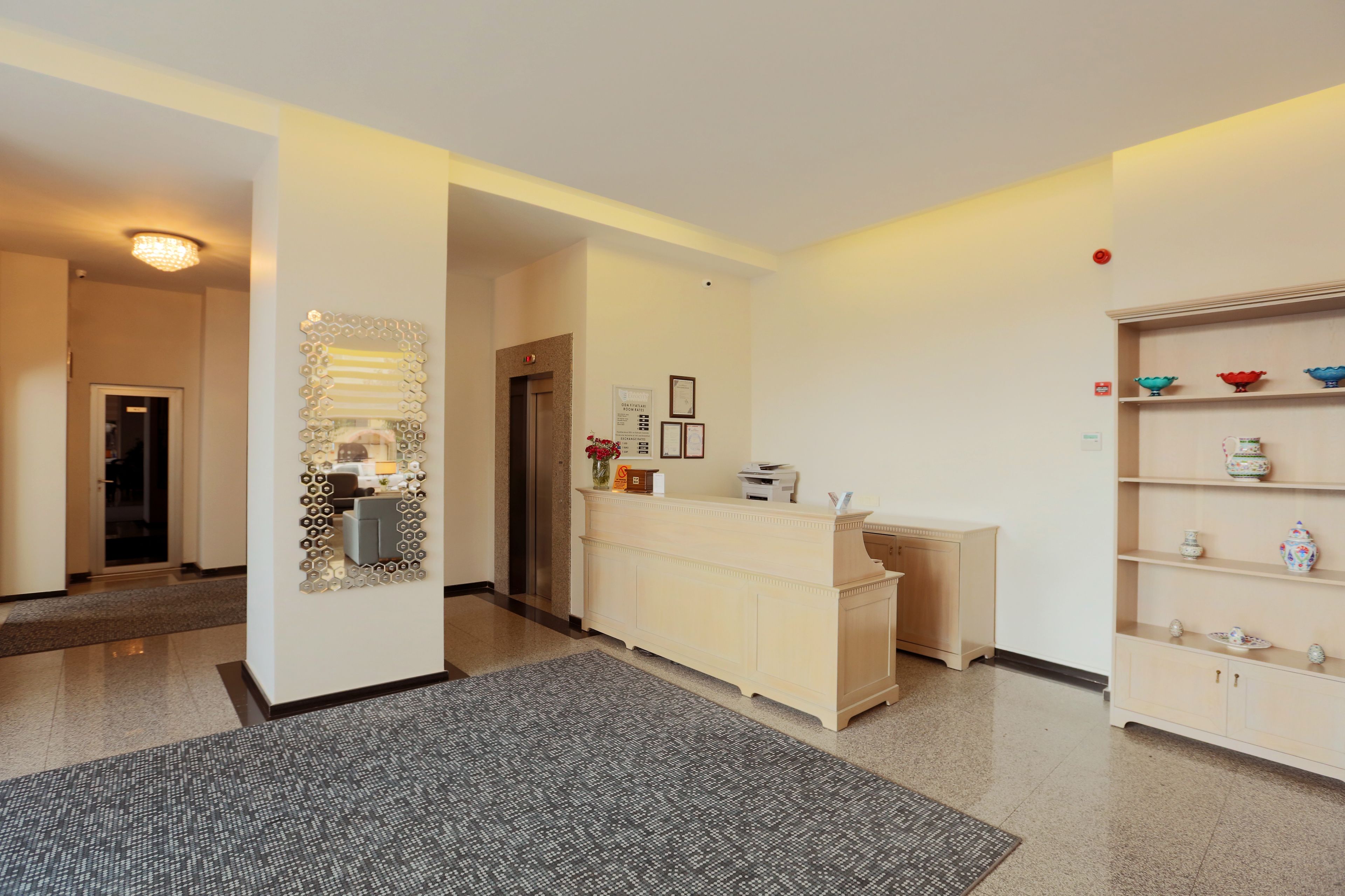 A reception area with a reception desk, a wall-mounted decorative mirror, and a shelf with decorative items.