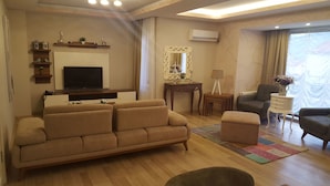 Ein Wohnzimmer mit einer Couch, einem Fernseher, einem kleinen Tisch mit einer Lampe und einem Sessel.