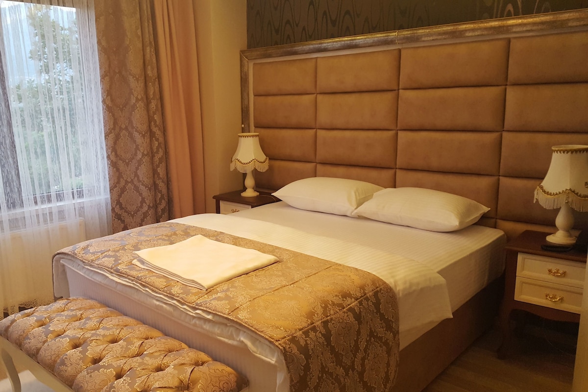 Uma cama bem arrumada com cabeceira, uma mesa de cabeceira com abajur e um banco no pé da cama.