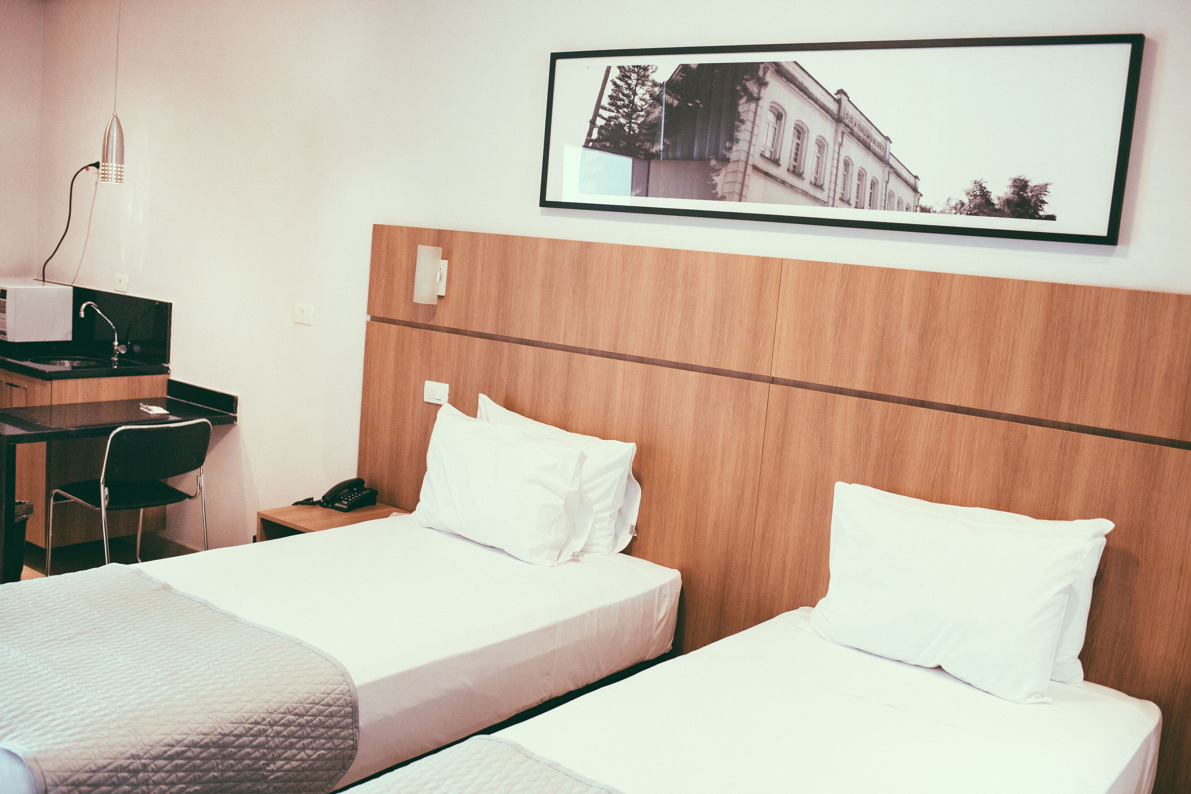 Una habitación de hotel con dos camas, un escritorio con teléfono y un cuadro en la pared.