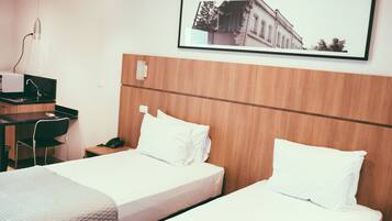 Una habitación de hotel con dos camas, un escritorio con teléfono y un cuadro en la pared.