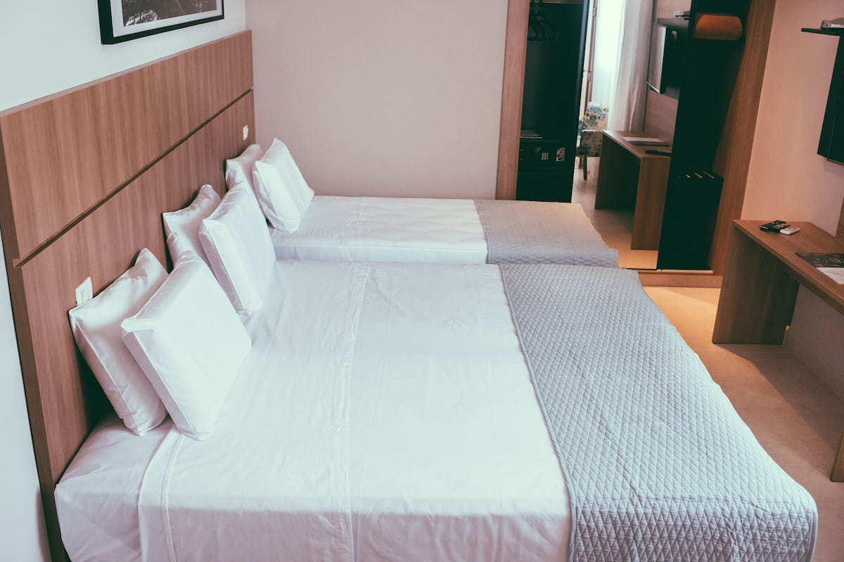 A hotel room with two single beds, a wooden headboard, a small desk, and a television.