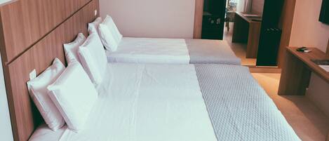A hotel room with two single beds, a wooden headboard, a small desk, and a television.