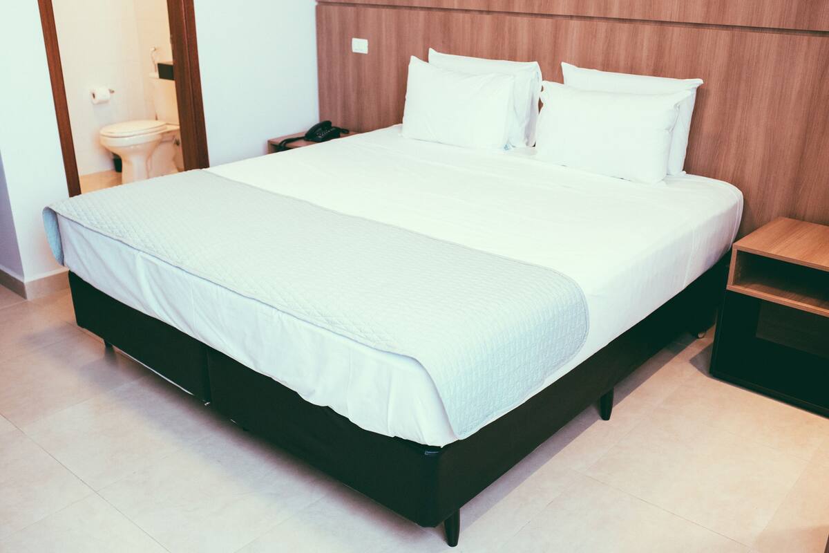 A neatly made bed with white linens and a wooden headboard in a hotel room.