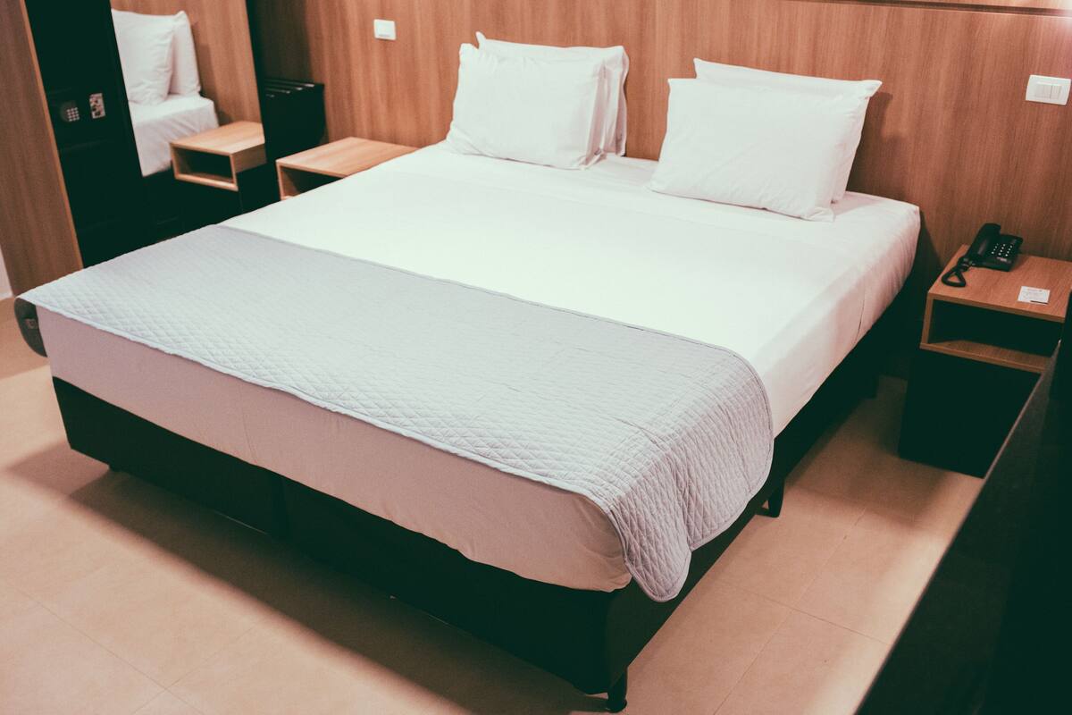 A neatly made bed with a white quilt, a wooden headboard, and a bedside table with a phone.