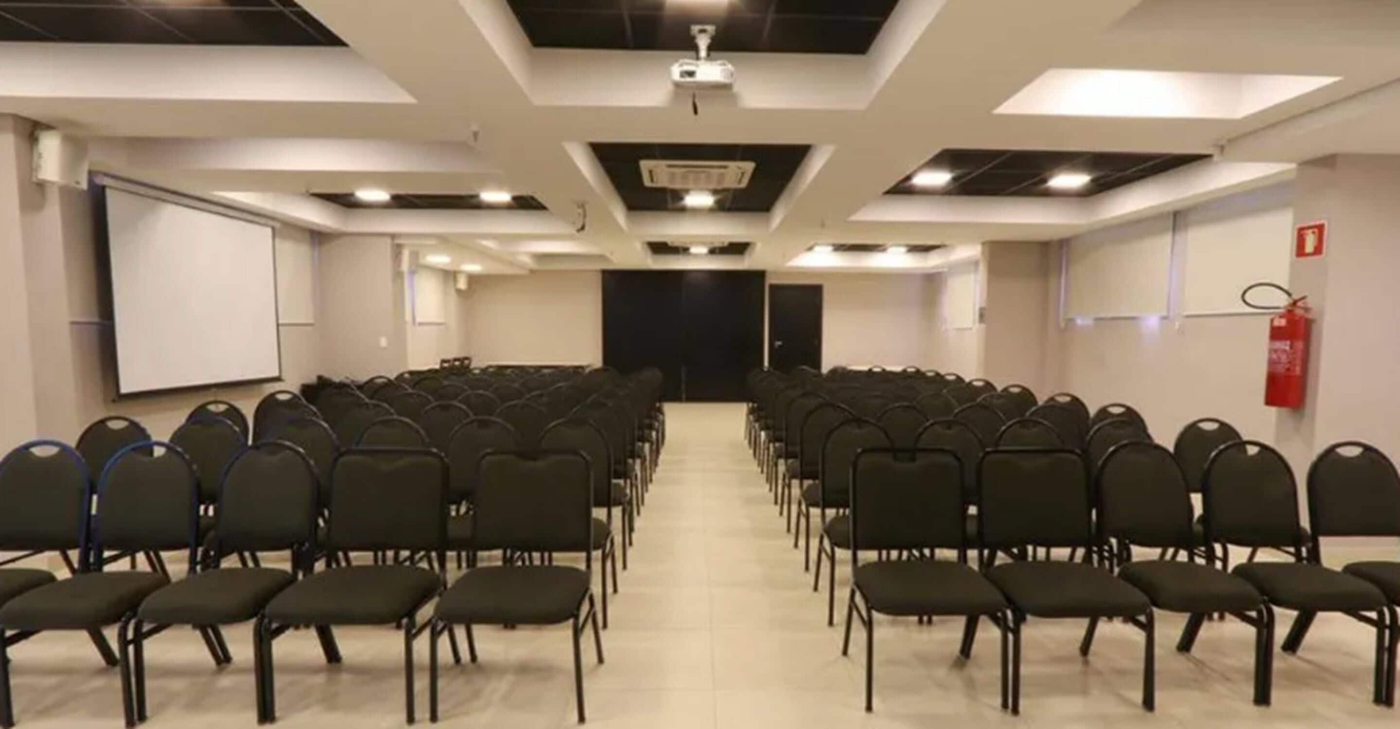 Ein Konferenzraum mit Reihen von Stühlen, einer Projektionsleinwand und einem Feuerlöscher.