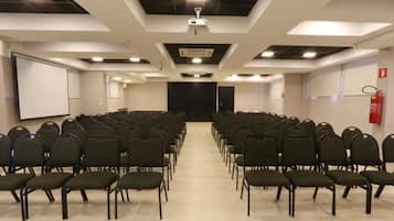 Un salón de conferencias con filas de sillas, una pantalla de proyector y un extintor.